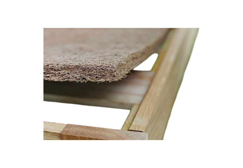 Close-up of a wooden frame with the CocoCoir Comfort Pad by Shepherd's Dream resting on top, showcasing its textured, woven coconut coir design. The focus is on the corner of the frame and the edge of the pad, emphasizing the contrast between the smooth wood and its rough texture.