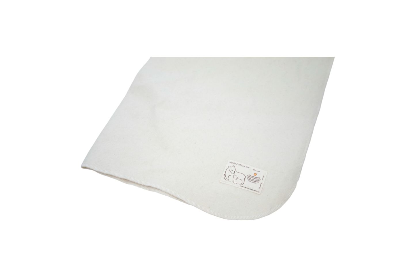 The Washable Wool Crib Mattress Protector by Shepherd's Dream, made from natural wool in a soft off-white hue, includes a small tag with a simple line drawing of an animal and text. Displayed against a black background, it serves as an elegant addition to any baby bedding collection.