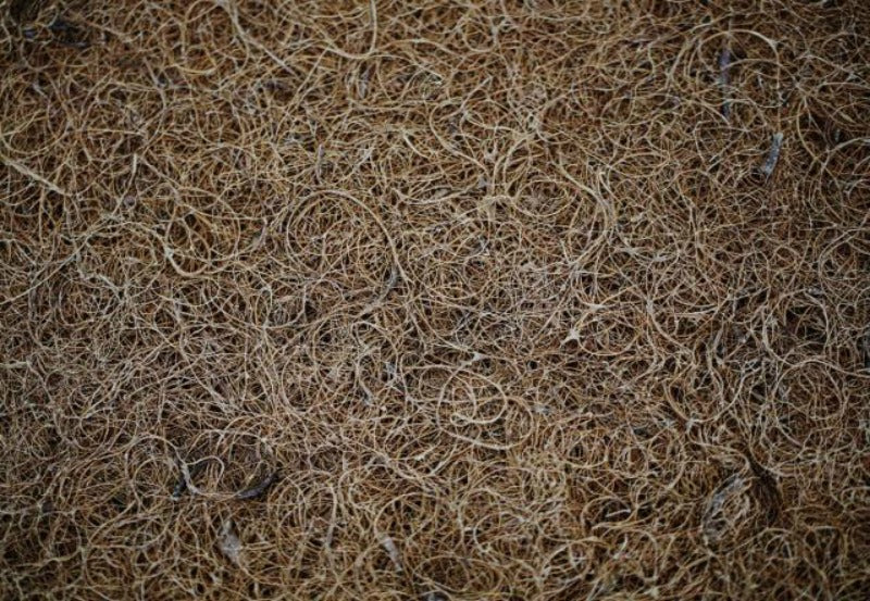 Close-up of a textured surface covered in a dense network of tangled, dry brown fibers, resembling the intricate weave of a Shepherd's Dream CocoCoir Comfort Pad.