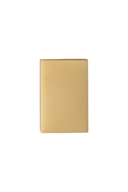 A plain, square-shaped, tan soap bar with smooth edges and minimal texture, set against a solid black background. Infused with Lemon Basil essential oil, the simple design and neutral color give the Violet and Lemon Basil A2/A2 Milk Soap - Regenerative Tallow® by Summer Solace Tallow a clean and minimalist appearance.