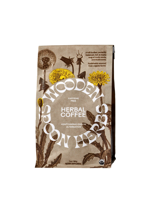 A brown and cream-colored packaging of WOODEN SPOON HERBS Herbal Coffee is shown, adorned with botanical illustrations that include dandelions. The text emphasizes that this caffeine-free blend contains adaptogenic mushrooms and serves as a coffee alternative. The net weight is 7 oz (198 g).